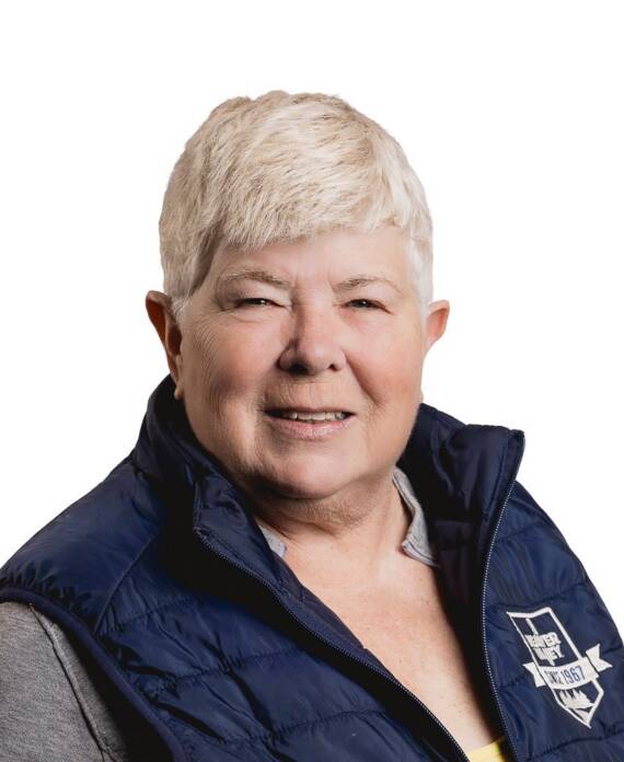Portrait of a smiling senior woman with short white hair, wearing a navy quilted vest with a logo patch on the chest.