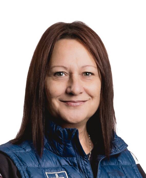 Smiling woman with shoulder-length brown hair wearing a blue quilted vest, looking at the camera.