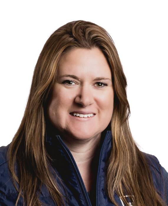 Smiling woman with long brown hair wearing a navy zip-up vest against a white background (head-and-shoulders portrait).