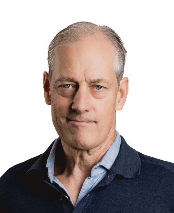 Head-and-shoulders portrait of a middle-aged man with light hair, wearing a blue collared shirt under a dark navy sweater, neutral expression.