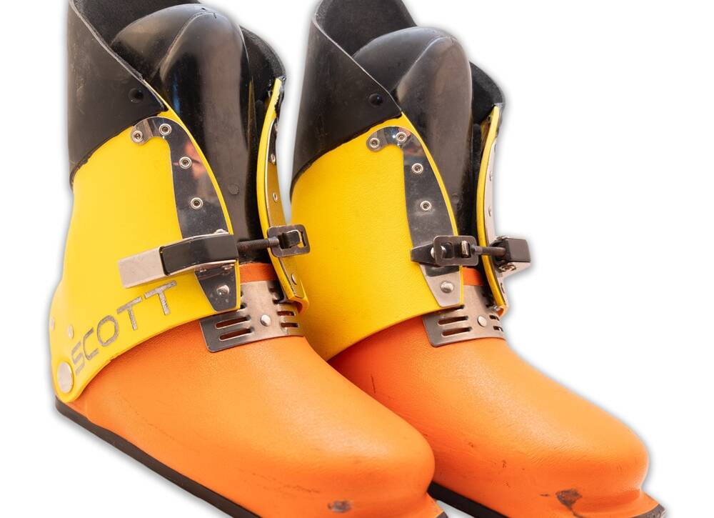 Pair of bright orange and yellow ski boots with black upper cuffs, buckles, and metal hardware shown on a white background.