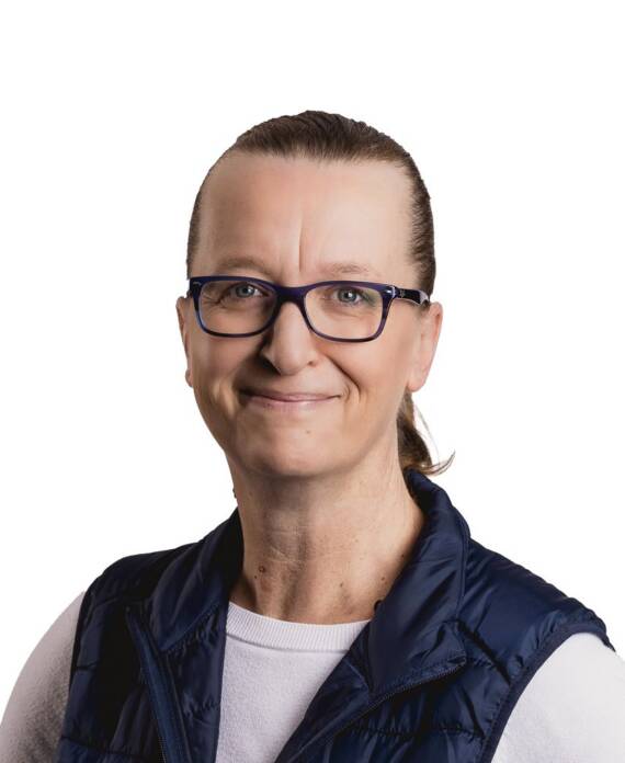 Smiling woman with dark frames and a ponytail, wearing a white top and navy puffer vest against a white background